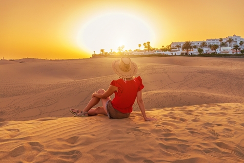 A tourist woman with a sunhat in Maspalomas Dunes of Gran Canaria sunset.