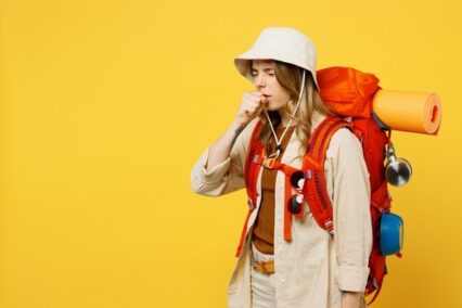 Side view young sick woman carry backpack with stuff mat cough cover mouth isolated on plain yellow background.