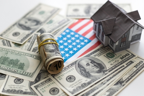 A toy house made of wood with a roof costs money, on a hundred-dollar bill.