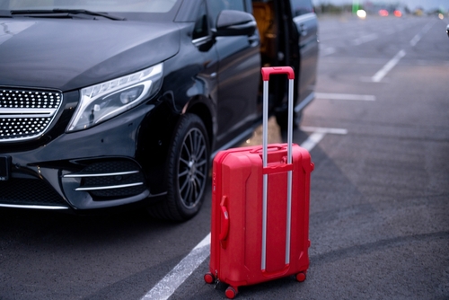 Red suitcase on parking lot near car.