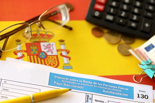 Modelo 130 spanish tax form for personal income tax for employers and professionals in direct evaluation instalments lies on flag of Spain close up on accountant table