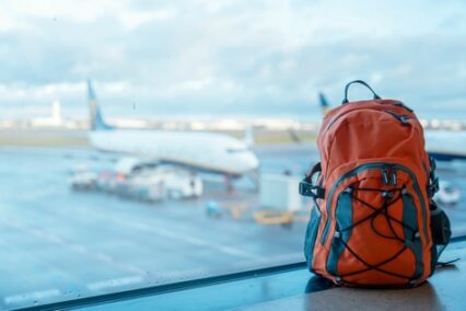 Orange backpack in an airport against a plane.