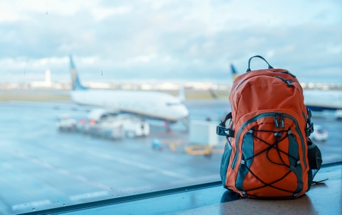 Orange backpack in an airport against a plane.