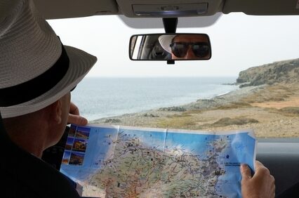 Tourist in rental car looks at the map while driving on the coast.
