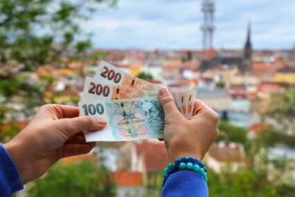 Hands holding Czech koruna paper money with Prague city skyline in background. Czech Republic cash.