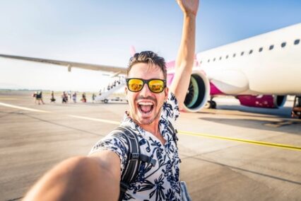 Happy young man taking selfie picture with smart mobile phone in front of airplane