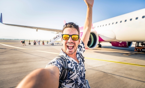 Happy young man taking selfie picture with smart mobile phone in front of airplane