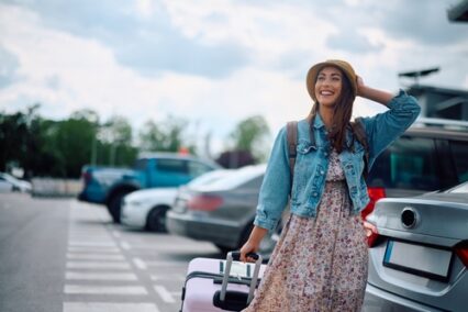 Carefree woman with luggage on parking lot at the airport.