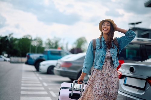 Carefree woman with luggage on parking lot at the airport.
