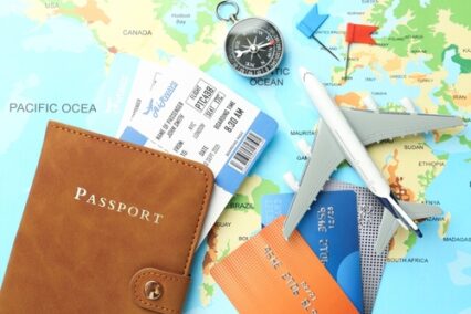 Passport in brown cover, airline tickets, airplane model, compass, credit card and small flags on world map, flat lay