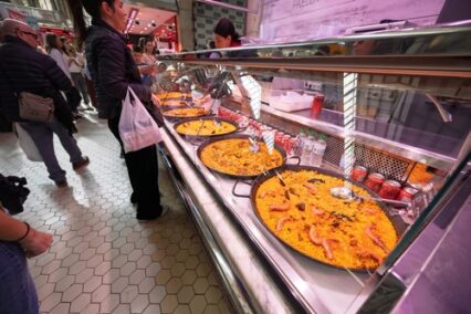 Interior of Mercado Central in Valencia bustling with people shopping for fresh produce under an iron and glass dome with modernist architectural elements