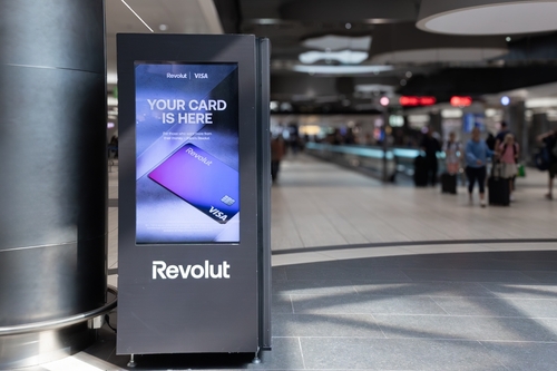 Modern digital signage displaying a vibrant credit card of online bank Revolut advertisement in a bustling airport terminal
