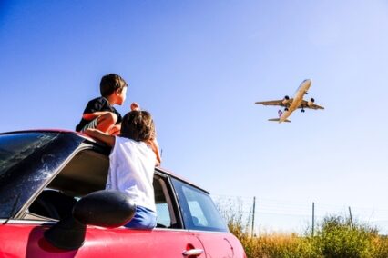 Two children, sat in a car, looking at a plane landing in Mallorca, Spain