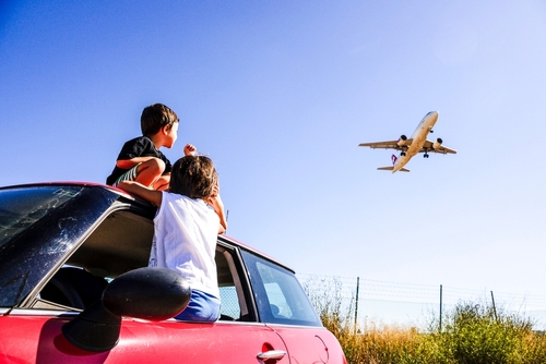 Two children, sat in a car, looking at a plane landing in Mallorca, Spain