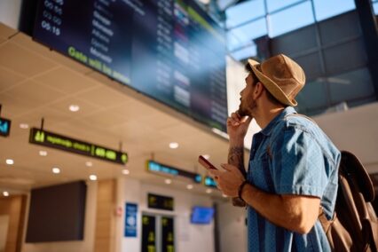 Male tourist checking flight departure at information board at airport.