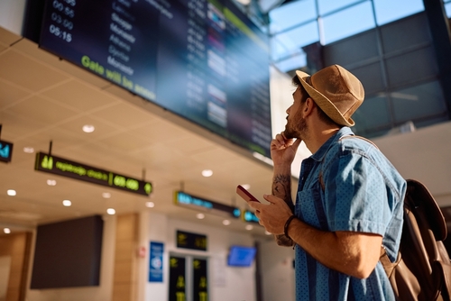 Male tourist checking flight departure at information board at airport.