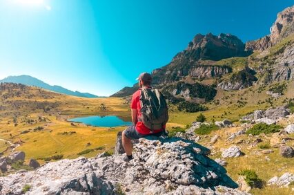 Man hiking rocky path at Ibón de Piedrafita, surrounded by high peaks and dramatic mountain terrain in the Aragonese Pyrenees with Peña Telera in the background