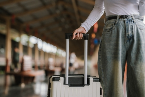 Stylish young woman traveling train station with suitcase, traveling alone on vacation or business trip, enjoying summer city adventure.