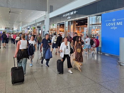 Travelers walking past shops and cafes inside the busy airport terminal at Málaga Airport, Málaga, Andalusia, Spain
