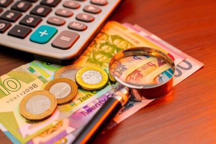 Image of a calculator, magnifying glass, and Ghanaian Cedi bills and coins resting on a wooden table