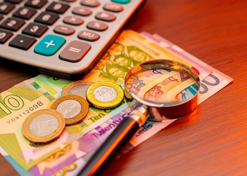 Image of a calculator, magnifying glass, and Ghanaian Cedi bills and coins resting on a wooden table