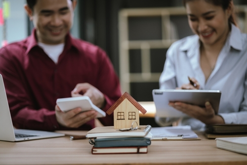 Real estate professionals with a calculator and a tablet next to a model house and keys, preparing for a property closing in India