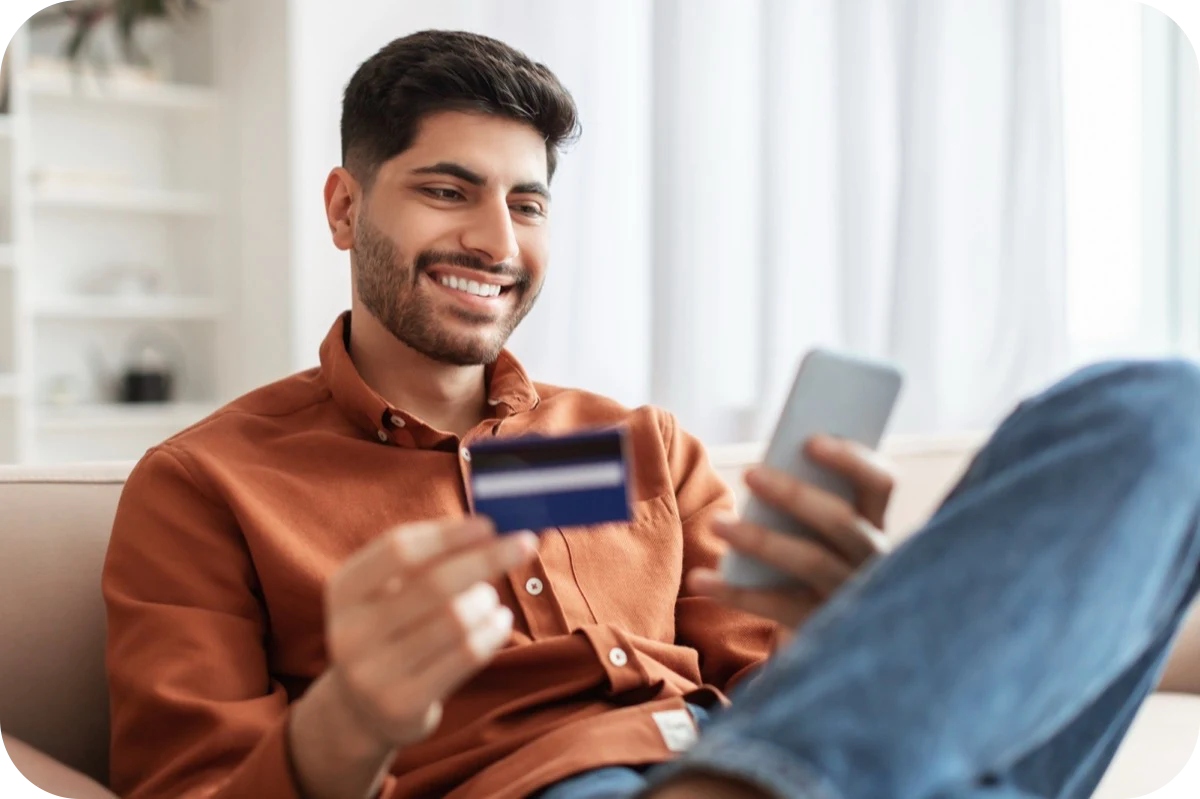 Smiling man on a couch holding a bank card and his phone