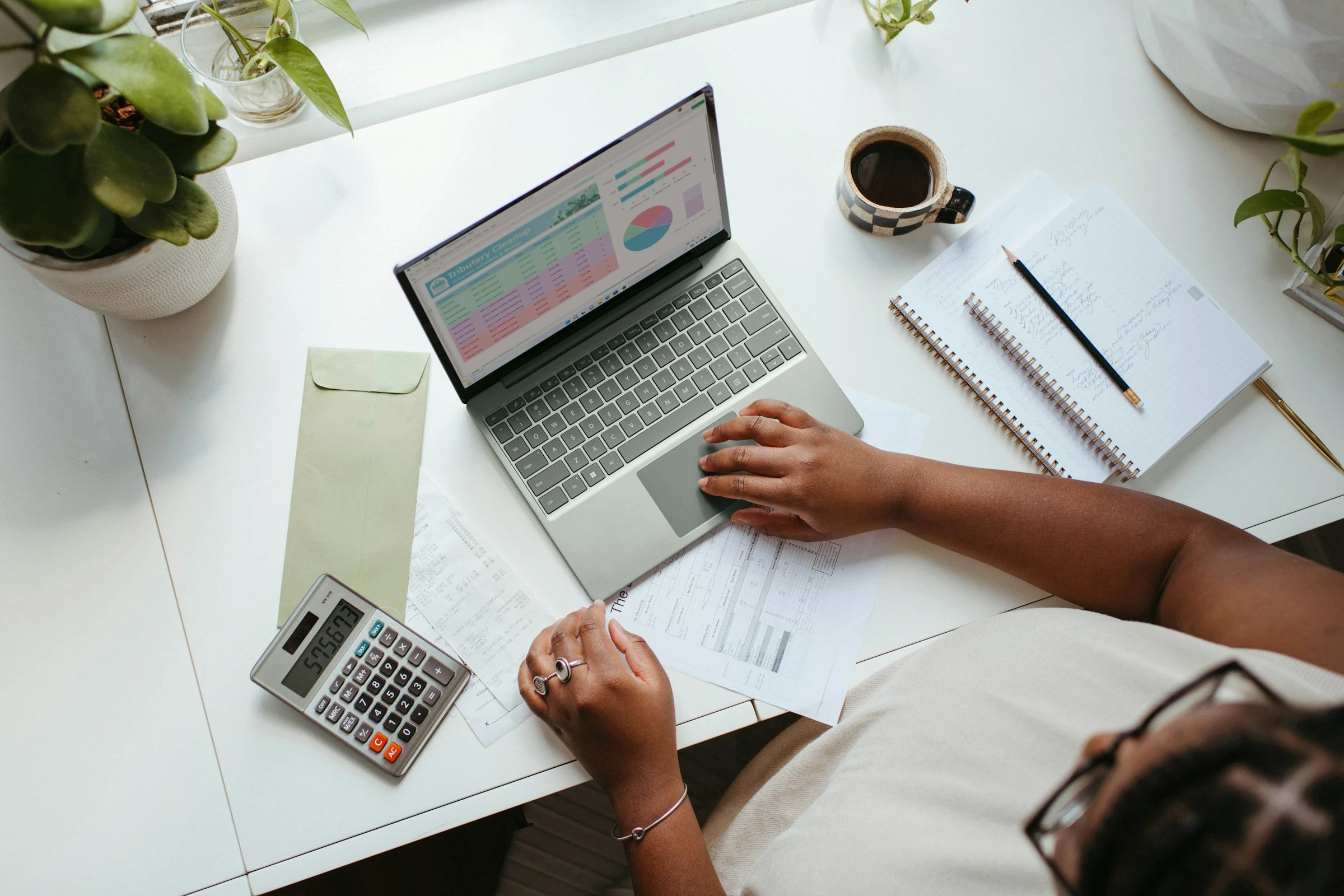 Person at a desk with a laptop, calculator and notebook, working through business paperwork.