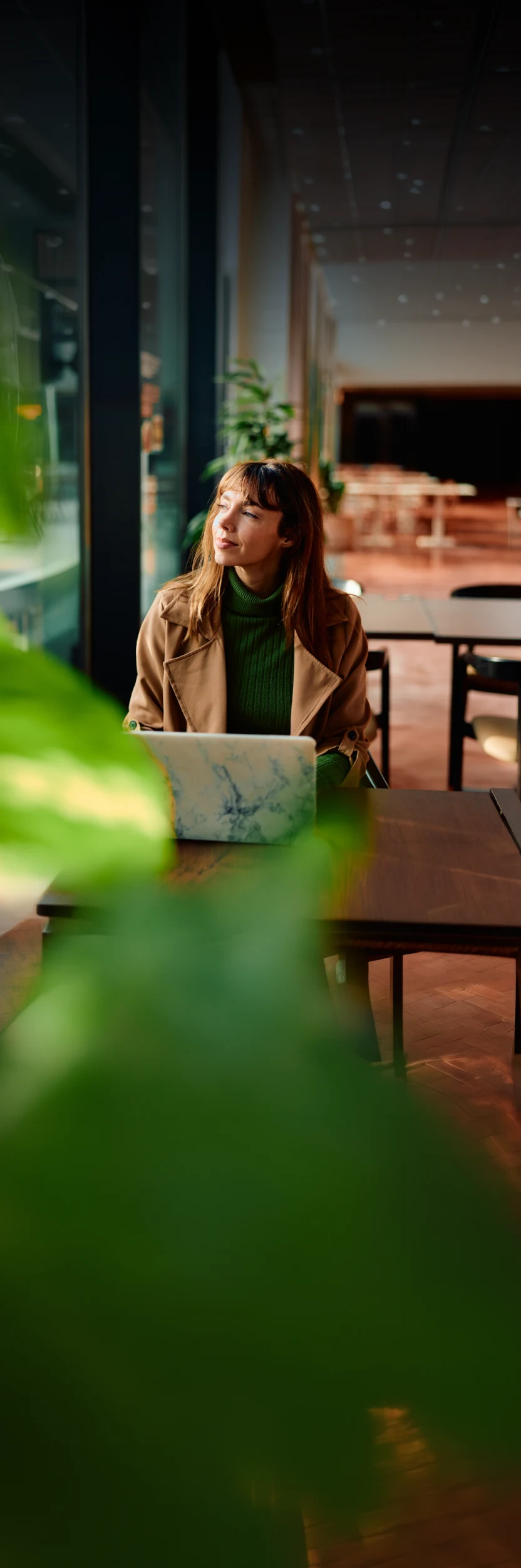 Business owner sitting at a cafe table with a laptop, looking out the window