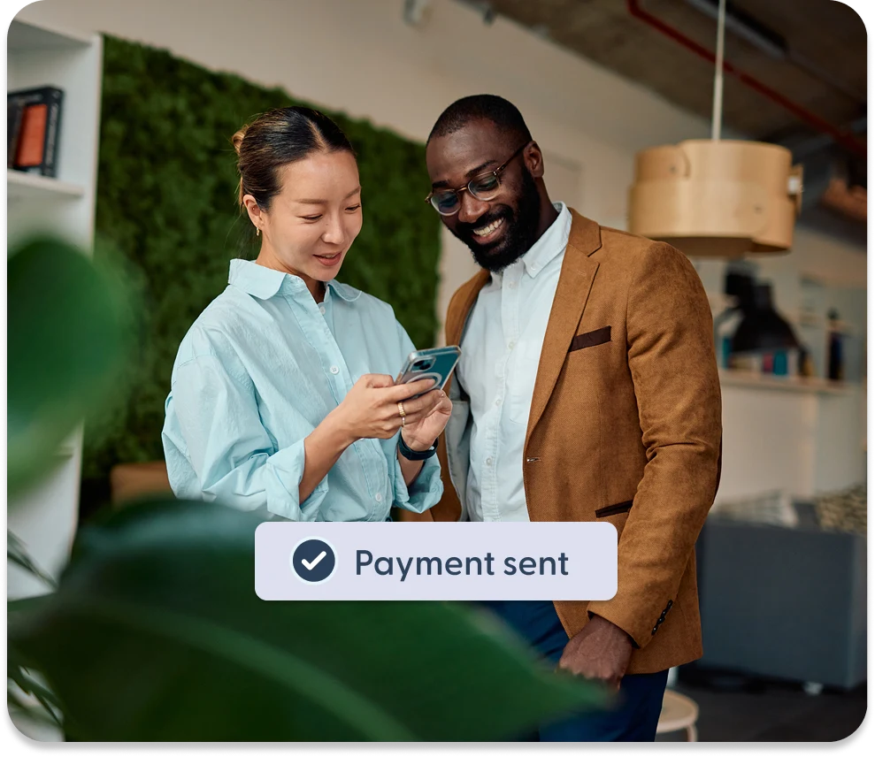 Two colleagues looking at a phone showing a “Payment sent” confirmation