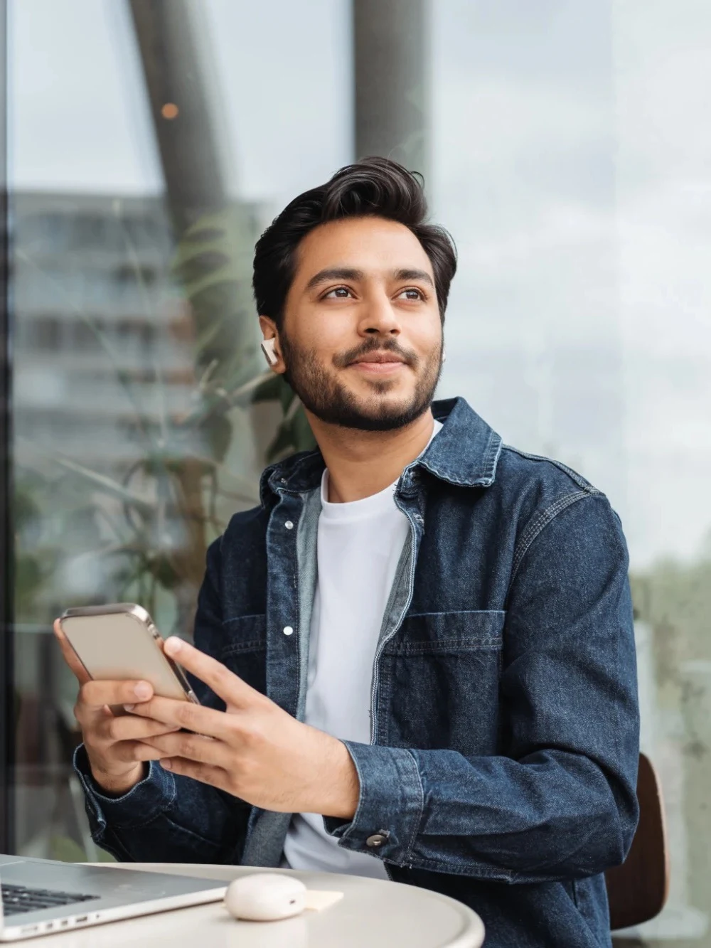 Man in a denim jacket holding his phone at a cafe table