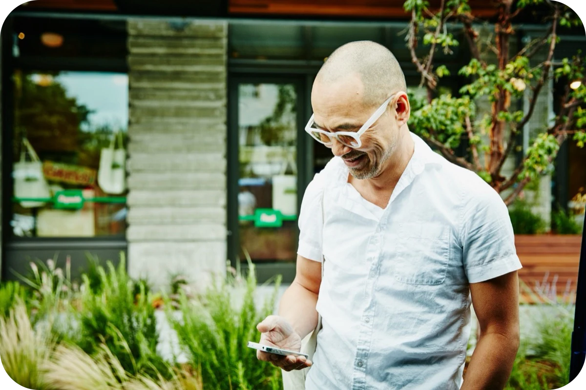 Smiling man in white glasses looking at his phone outside a shop