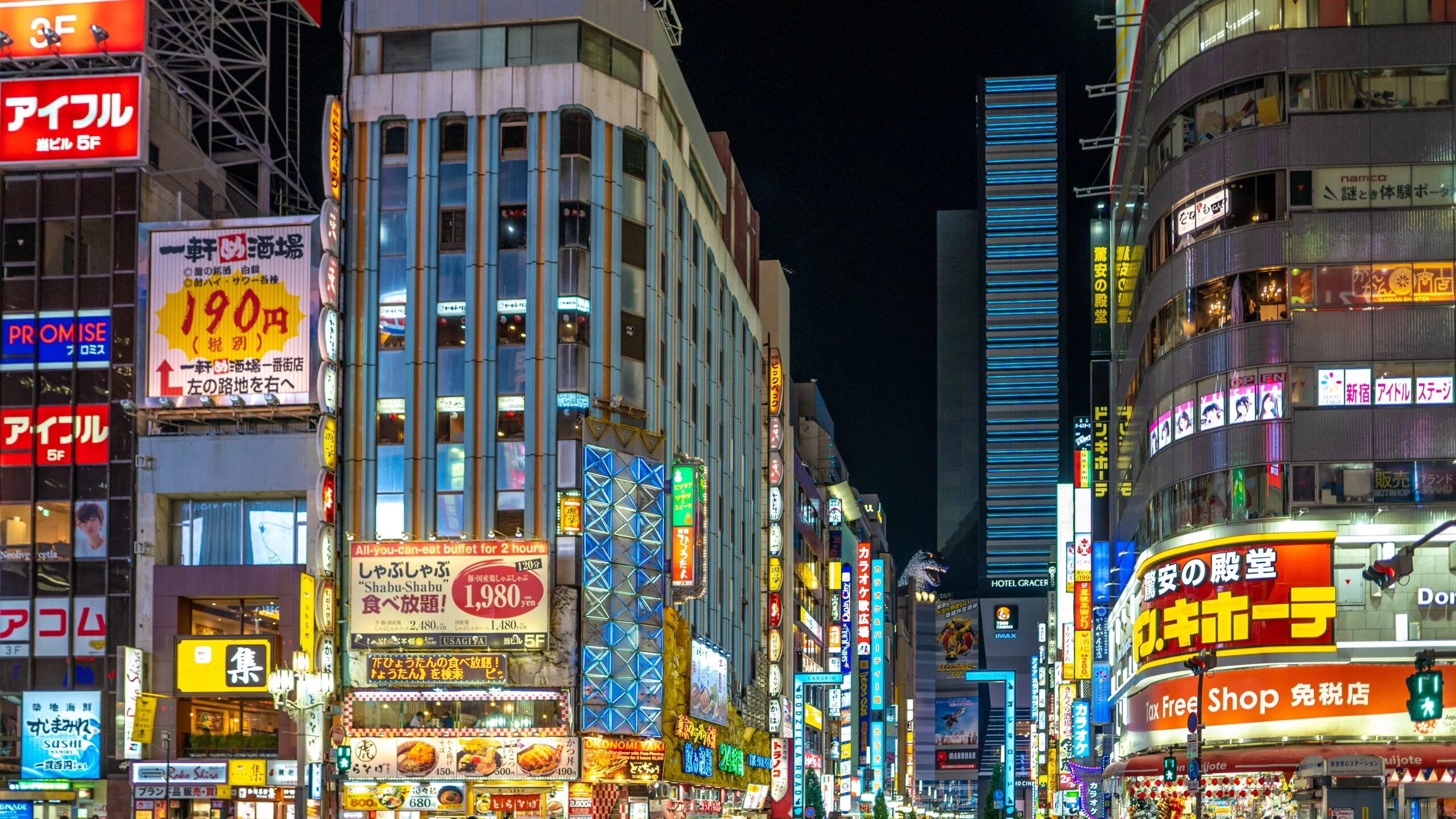 Neon-lit shop signs on a busy Tokyo street at night.